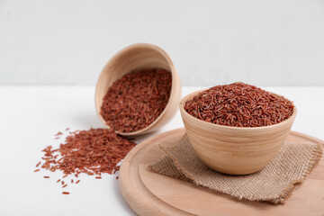 Wooden board with bowls of raw brown rice on white background