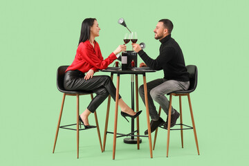Young couple with wine at restaurant table on green background