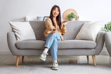 Obraz premium Young Asian woman with fried insects watching TV on sofa at home