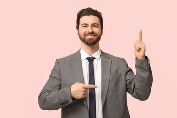 Young businessman pointing at something on pink background
