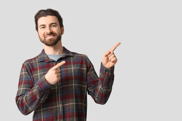 Young man pointing at something on light background