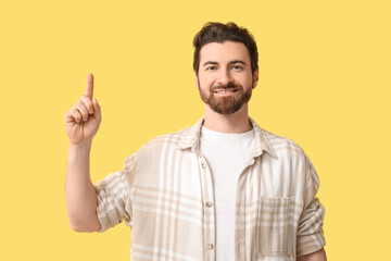 Fototapeta premium Young man pointing up on yellow background