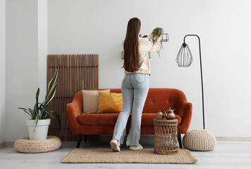 Young woman putting plant on shelf in living room, back view