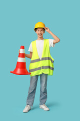 Teenage worker in hardhat with traffic cone on blue background
