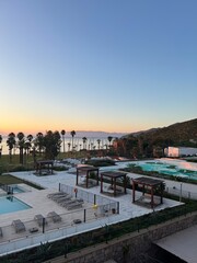 Fototapeta premium Beautiful sunset view over calm waters and resort pools near coastal palm trees