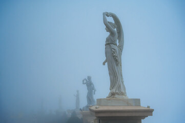 A marble statue of an ancient Roman or Greek goddess in a garden in a thick fog.