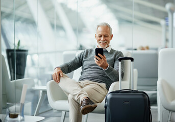 Elderly caucasian male relaxing at airport lounge with smartphone and luggage.