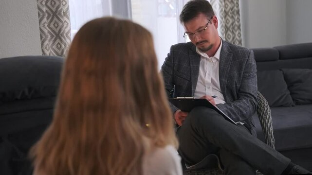 A psychiatrist evaluates a patient with obsessive compulsive disorder, documenting her symptoms and responses. As the woman shares her experiences, he offers focused and empathetic attention.