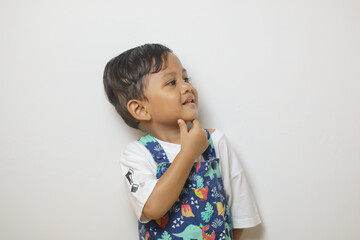 Thoughtful young boy with curly hair looking aside at copy space, touching chin in contemplation,...