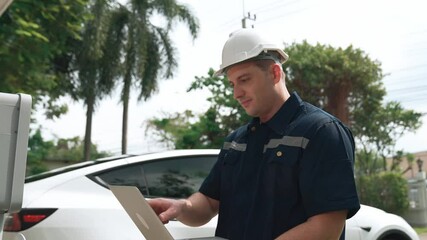 Qualified technician working on home EV charging station installation, making troubleshooting and configuration setup on charging system with laptop for EV at home. Fastidious