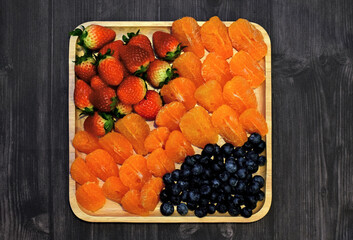 Strawberries, oranges and blueberries on a wooden tray and wood grain background.