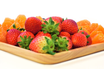 Strawberries, oranges and on a wooden tray and white background.