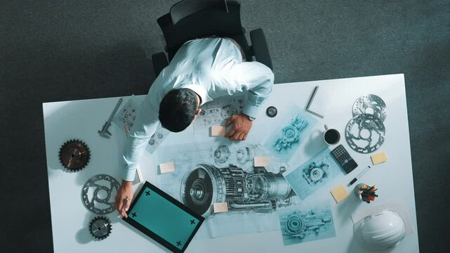 Top down view of skilled engineer writing and planning turbine engine design while sitting at meeting table with gear and electronic generator scatter around. Technician taking a note. Alimentation.