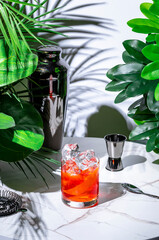 Non-alcoholic negroni or nagroni cocktail or mocktail drink with alternative gin, non-alcoholic red vermouth and aperitif. White marble table with tropical leaves