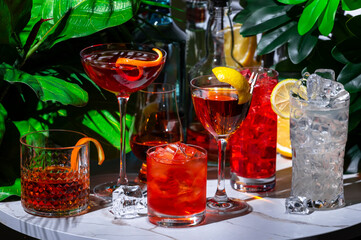 Summer alcoholic cocktail party with ready-made cocktails, bar tools and bottles of spirits on marble table with green plants