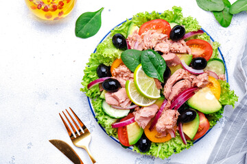 Keto salad with tuna, avocado, black olives, vegetables, lettuce and olive oil and lime dressing. White background, top view