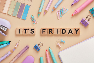 Words It's Friday made of wooden blocks with colorful pastel stationery on a beige background