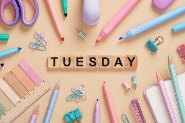 Word Tuesday made of wooden blocks with colorful pastel stationery on a beige background