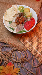 Top view delicious Soup or Soto Betawi  with beef, potato, fresh tomato, lime slices, and fried shallot. Served in white bowl with unique decoration. Space for text available