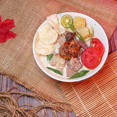 Top view delicious Soup or Soto Betawi  with beef, potato, fresh tomato, lime slices, and fried shallot. Served in white bowl with unique decoration. Space for text available