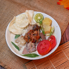 Soup or Soto Betawi with savory coconut milk broth filled with pieces of potato and beef is a traditional Indonesian food typical of Jakarta. Served in a white bowl on bamboo mat and burlap