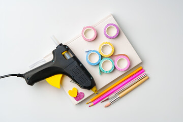 Craft supplies arranged on a table with a glue gun, washi tape, and colored pencils ready for a...