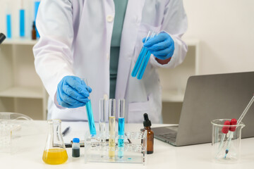 Fototapeta premium Cute Caucasian schoolgirl wearing white scientist outfit holding two test tubes filled with blue liquid in science classroom. carefully handling chemical substances while wearing protective gloves.