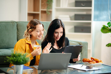 Two women collaborating on a project at home, brainstorming with a laptop and notebook in a cozy setting.