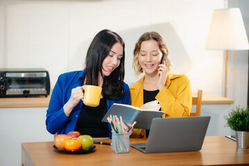 Two professional women collaborating on a business project with a laptop, notebook, and coffee at home.