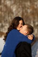 man and woman hugging. The woman is wearing a blue knitted sweater, has long dark hair, and is smiling.