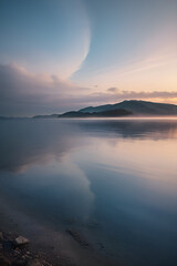 Fototapeta premium Serene Sunset Over Water - Tranquil Landscape with Ocean and Mountains