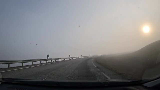 Driving through the tundra in northern Norway on E69 road. Winding roads with grassy hills, patches of snow, and dense fog gradually clearing as sunlight breaks through.