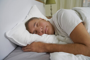 Man peacefully sleeping in a cozy bedroom during the morning hours with soft light filtering...