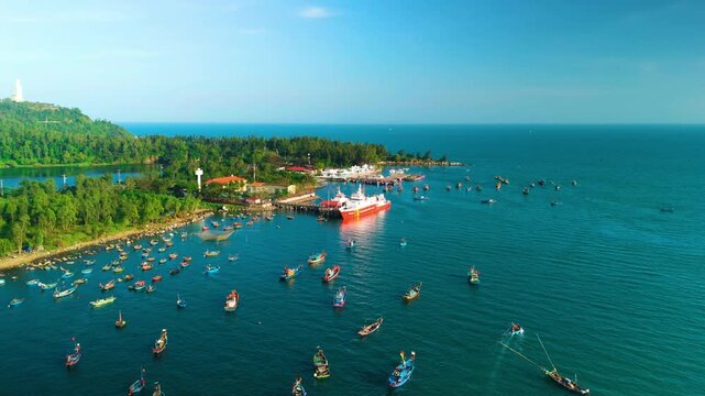 Colorful fishing boats navigating coastal waters near vung tau, vietnam, with large red white cargo vessel anchored alongside pier under bright blue sky