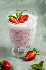 Strawberry chia pudding in a stemmed glass garnished with yogurt, strawberry halves and mint leaves...