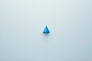 Fototapeta premium A solitary blue triangular prism resting on a smooth light background, showcasing minimalist design