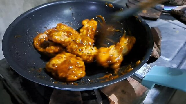 Asian woman stirring crispy chicken with ava sauce in a frying pan.