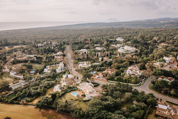 Aerial view of a residential area surrounded by lush greenery, with the coastline and the Rock of Gibraltar visible in the distance.