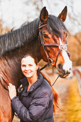 A young woman stands with her saddled horse model between the wooden fences of the outdoor paddocks...