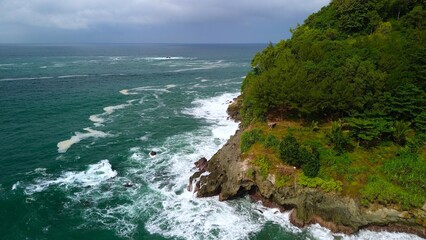 Aerial drone view of coastline with hills and trees, as well as view of coral cliffs and sea with waves from the ocean in Lampon Kebumen Central Java Indonesia