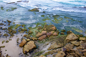 A vibrant scene at Bondi Beach, capturing people enjoying the sun, sand, and surf. Rocks frame the shore, with golden sand stretching out, epitomizing beach bliss and lively summer fun.