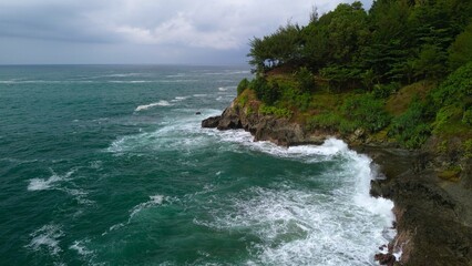 Aerial drone view of coastline with hills and trees, as well as view of coral cliffs and sea with waves from the ocean in Lampon Kebumen Central Java Indonesia