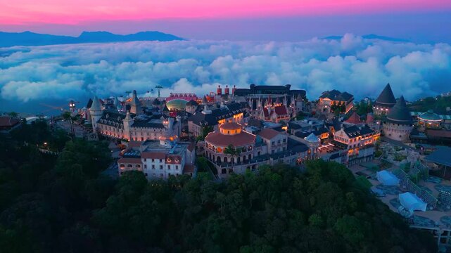 Aerial view is lunar castles of Bana Hills at pink sunset time with clouds down. The famous tourist destination of Da Nang, Vietnam. Near Golden bridge.