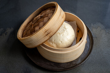Steamed bao bun in bamboo basket on dark plate
