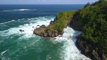 Aerial drone view of coastline with hills and trees, as well as view of coral cliffs and sea with waves from the ocean in Lampon Kebumen Central Java Indonesia