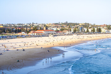 Stunning Bondi Beach scene with crystal-clear ocean water and happy beachgoers. The vibrant blue waves meet the bustling city skyline of modern buildings in the background.