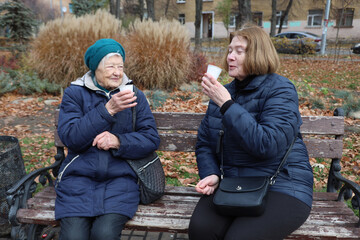 Two elderly ladies, mother and daughter, walking around the city, talking, laughing, drinking coffee. Active healthy lifestyle