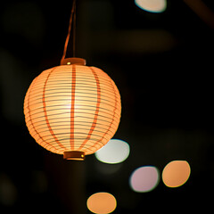 Illuminated paper lantern hanging at night, soft focus bokeh background