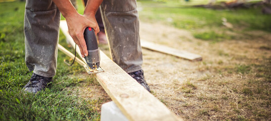 Man uses an electric saw to cut a plank. Close-Up of a Carpenter's Hands Operating a Power Saw on Wood