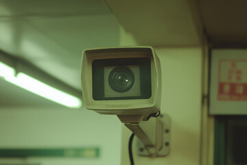 Surveillance Camera in Subway Station: An off-white security camera mounted on a wall in a dimly lit subway station, its lens focused, symbolizing security and surveillance.